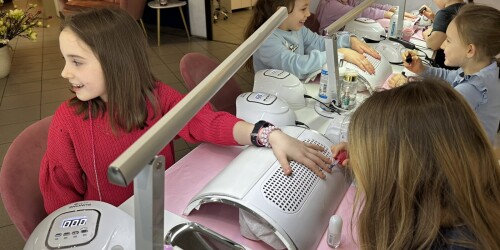 Uczennice klasy 2c na stanowiskach manicure i malują paznokcie – jedne zajmują stanowisko manikiurzystki, drugie klientki.