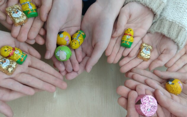 Zdjęcie 1 przedstawia dłonie dzieci na których leżą jajka czekoladowe w zielono-żółtym opakowaniu