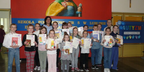 Na zdjęciu stoi w dwóch rzędach grupa uczniów oraz Pani Dyrektor i nauczyciel bibliotekarz. Dzieci trzymają w rękach nagrody  i dyplomy.
