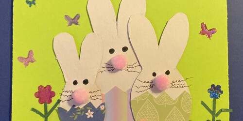 5. Kartka wielkanocna – trzy króliki wycięte z papieru, wyłaniające się z kolorowych skorupek jajek. Obok kwiaty.