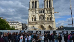 Dziewczynki i chłopcy wraz z opiekunami stoją przed Katedrą Notre-Dame.