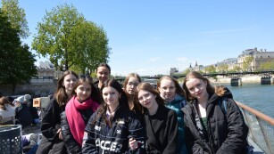 Grupa dziewczynek stoi na statku płynącym po Sekwanie w tle zabytkowy most w Paryżu.